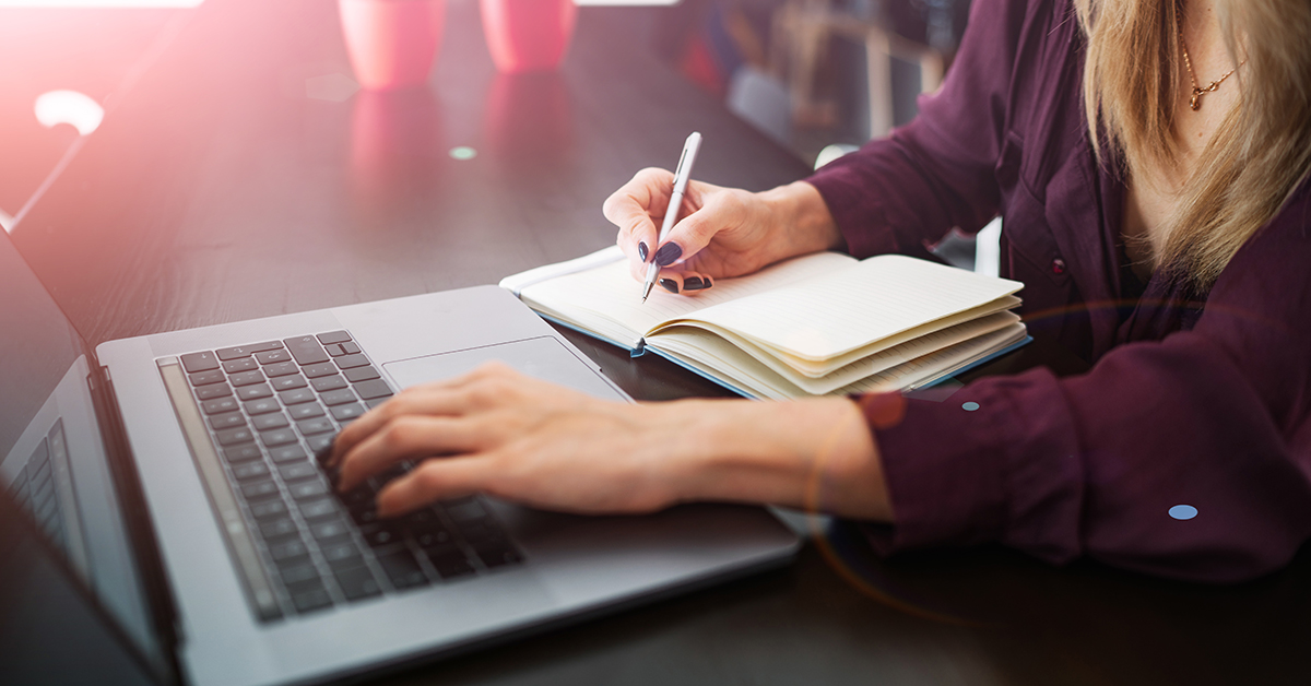 Woman taking notes while working on a computer